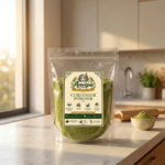 A premium pouch of Anvipa chemical-free Pure Coriander Powder beside a small wooden bowl filled with cold ground pale-golden dhania powder.