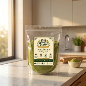 A premium pouch of Anvipa chemical-free Pure Coriander Powder beside a small wooden bowl filled with cold ground pale-golden dhania powder.